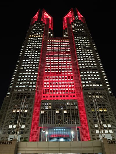 結核予防運動シンボルマークである「複十字」のイメージカラー「赤色」にライトアップされた東京都庁第一本庁舎